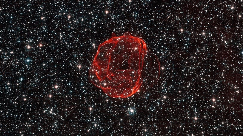  A wispy red bubble of matter on a dense background of stars. A Hubble image of a supernova. 