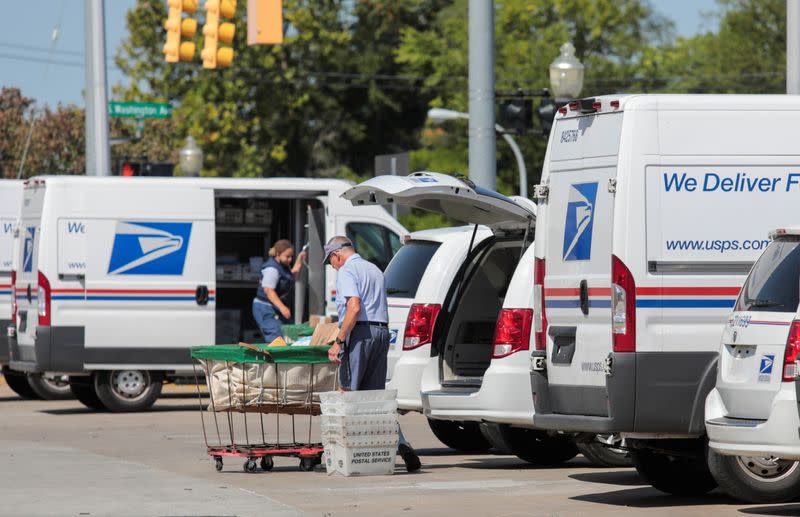 United States Postal Service (USPS) workers load mail into delivery trucks outside a post office in Royal Oak