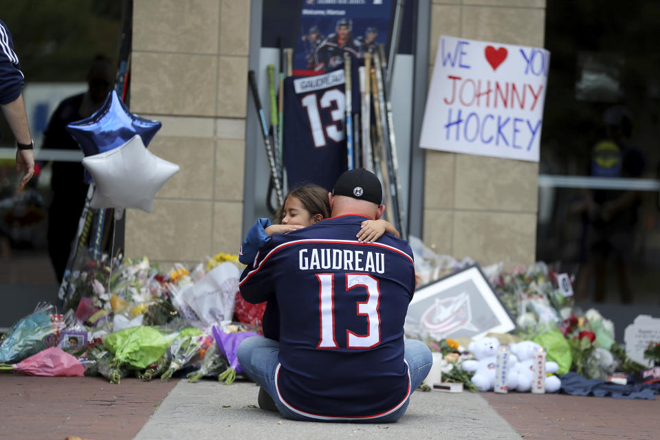 Shiloh Rivera, facing, mourns with Hylas Stemen of Columbus, at the makeshift memorial set up by fans for Blue Jackets hockey player Johnny Gaudreau in Columbus, Ohio, Friday, Aug. 30, 2024. Gaudreau, along with his brother Matthew, was fatally struck by a motorist while riding his bicycle on Thursday. (AP Photo/Joe Maiorana)