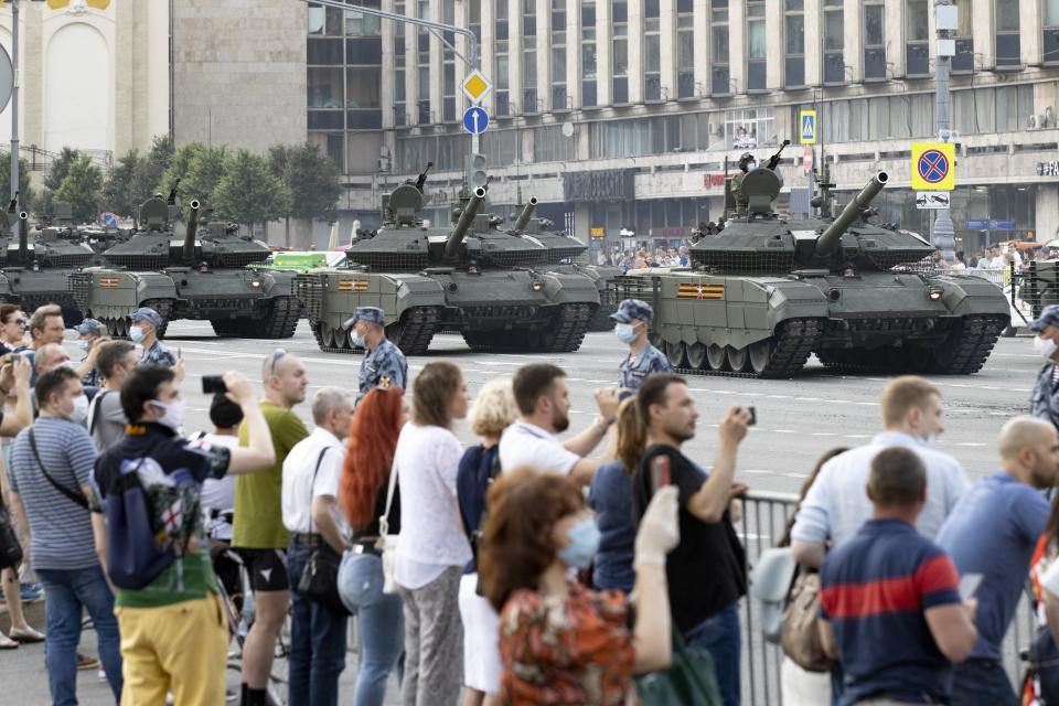 FILE - In this file photo taken on Wednesday, June 17, 2020, people, same of them wearing face a masks, glasses and gloves to protect against the coronavirus watch as Russian military vehicles roll along Tverskaya street toward Red Square during a rehearsal for the Victory Day military parade in Moscow, Russia. A massive military parade that was postponed by the coronavirus will roll through Red Square this week to celebrate the 75th anniversary of the end of World War II in Europe, even though Russia is continuing to register a steady rise in infections. (AP Photo/Alexander Zemlianichenko, File)