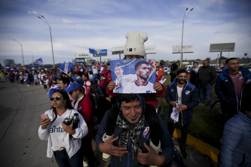 Una niña sostiene una foto de Luis Suárez al ser alzada por su padre afuera del aeropuerto durante el recibimiento al delantero, el domingo 31 de julio de 2022. Suárez jugará con Nacional de Montevideo. (AP Foto/Matilde Campodónico)