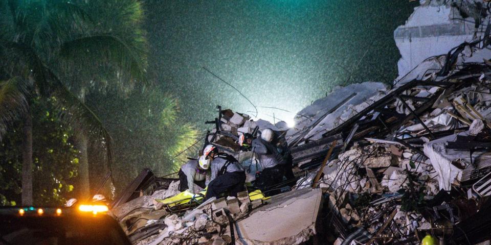 Search and rescue workers pull a body from the rubble of Champlain Tower at night.