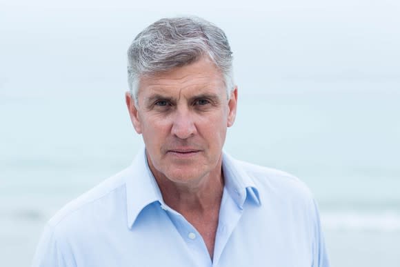 Older man in blue shirt outdoors with serious expression on his face.