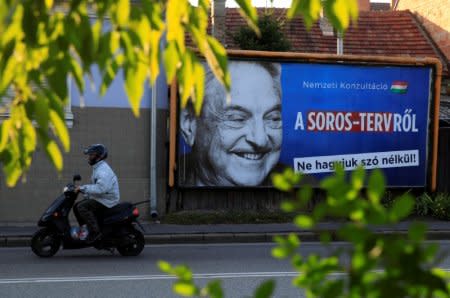 FILE PHOTO: A man rides his moped past a government billboard displaying George Soros in monochrome next to a message urging Hungarians to take part in a national consultation about what it calls a plan by the Hungarian-born financier to settle a million migrants in Europe per year, in Szolnok, Hungary, October 2, 2017.  REUTERS/Bernadett Szabo