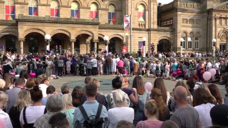 A crowd of people taking part in a vigil outside Southport's sandstone-coloured The Atkinson