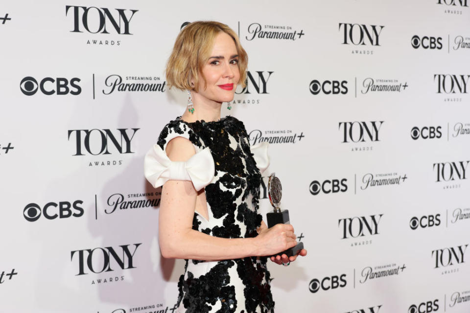 Sarah Paulson on the Tony Awards red carpet, holding a Tony Award. She is wearing a dress with floral patterns and puffed sleeve details