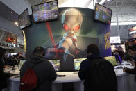 An image of "Crypto," the main character in the video game "Destroy All Humans!," appears above people playing video games at the THQ Nordic exhibit, Thursday, Feb. 27, 2020, at the Pax East conference, in Boston. (AP Photo/Steven Senne)