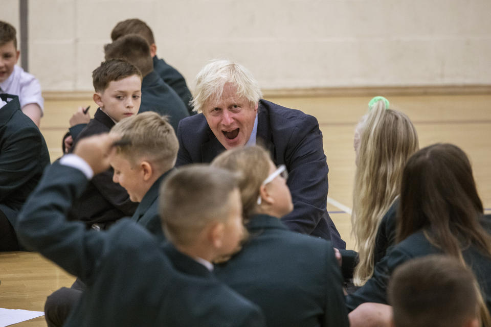 Britain's Prime Minister Boris Johnson reacts with children during a visit to Castle Rock school on the pupils' first day back, in Coalville, East Midlands, England, Wednesday, Aug. 26, 2020. Following mounting pressure to change tack, the British government decided late Tuesday to ditch its advice that high school students in England don’t need to wear face masks while at school. In another in a series of abrupt changes in coronavirus-related policy, the government said children in secondary schools — those above 11 years of age — in areas under local lockdown rules, such as Greater Manchester, will have to don face masks when moving around corridors and communal areas. (Jack Hill/Pool Photo via AP)