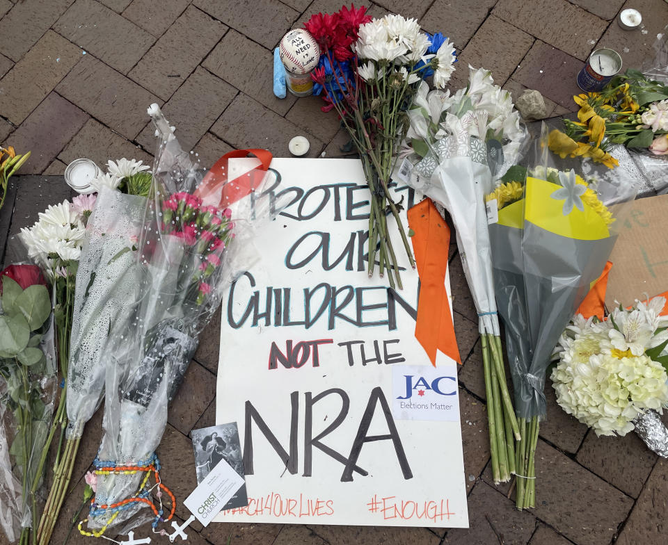 Flowers and candles lay on brick surface with sign reading Protect our children, not the NRA, #march4ourlives, #enough.