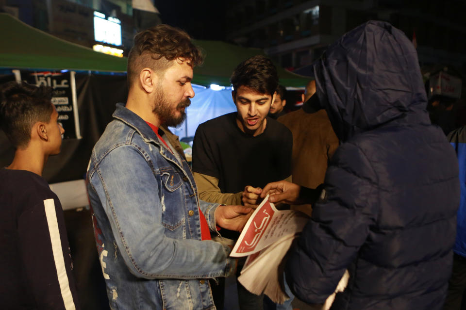 In this Tuesday, Nov. 19, 2019 photo, a masked man distributes copies of “Tuk Tuk” newspapers, in Tahrir Square in Baghdad, Iraq. A small group of Iraqi volunteers is working in secrecy to produce the newspaper that aims to be the voice of the largest grassroots protest movement in the country’s modern history. Its editors say the newspaper is vital amid shutdowns of the internet, filling a void left by mainstream Iraqi journalists who either back the government or fear retaliation. (AP Photo/Khalid Mohammed)