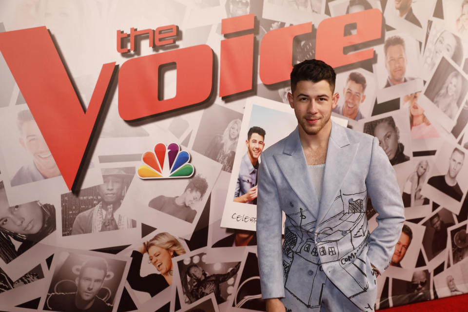 Nick Jonas poses in front of a screen advertising TV series The Voice.