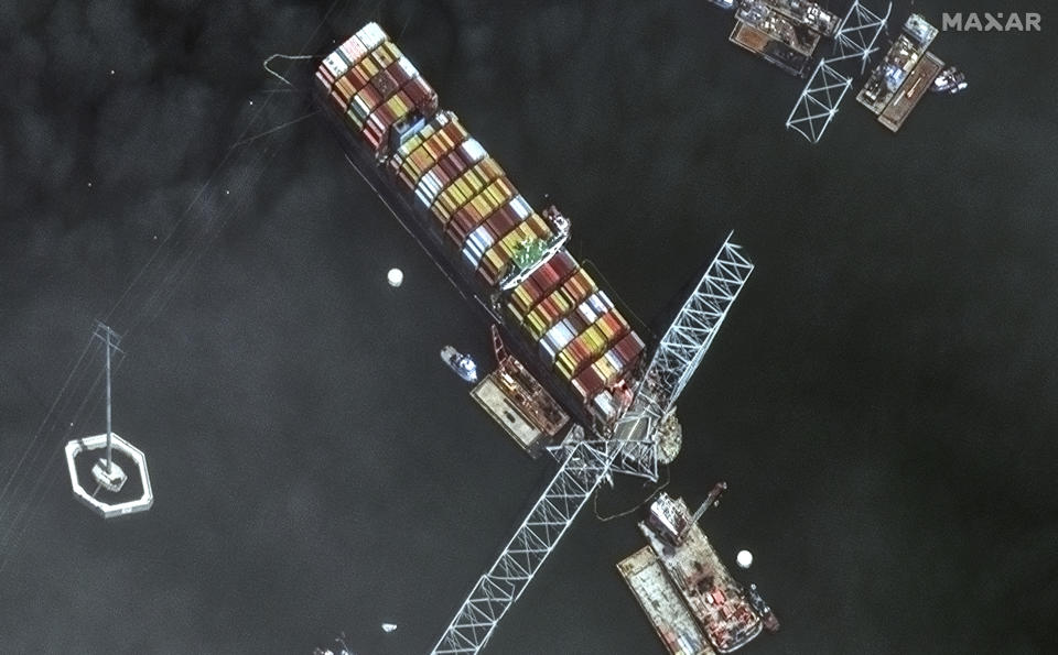 This satellite image provided by Maxar shows the bow of the container ship Dali remains stuck underneath sections of the fallen Francis Scott Key Bridge, while salvage crews and barges with cranes continue removing some of the bridge debris and hundreds of shipping containers still onboard the vessel, in Baltimore, Monday, April 8, 2024. (Satellite image ©2024 Maxar Technologies via AP)