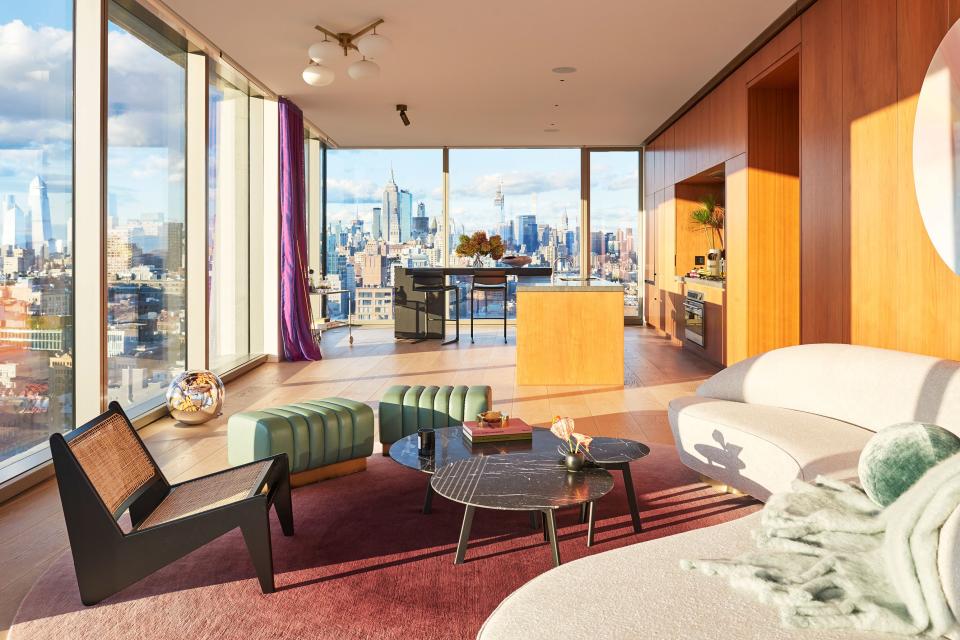 Rows of 10-foot-tall windows flood the space with sunlight during the day and Manhattan’s urban glitter at night, yet this abundance of glass can also feel cold. To add warmth, interior designer Armann Ortega filled the home with luminous colors and flowing silhouettes. The curvaceous sofa is Vladimir Kagan’s Serpentine model from Holly Hunt, and the round rug is a custom piece from Lepere.