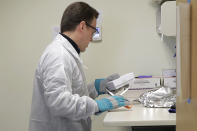 Pharmacist Michael Witte opens a package taken from a freezer that contains the potential vaccine for COVID-19, the disease caused by the new coronavirus, on the first day of a first-stage safety study clinical trial of the vaccine, Monday, March 16, 2020, at the Kaiser Permanente Washington Health Research Institute in Seattle. (AP Photo/Ted S. Warren)