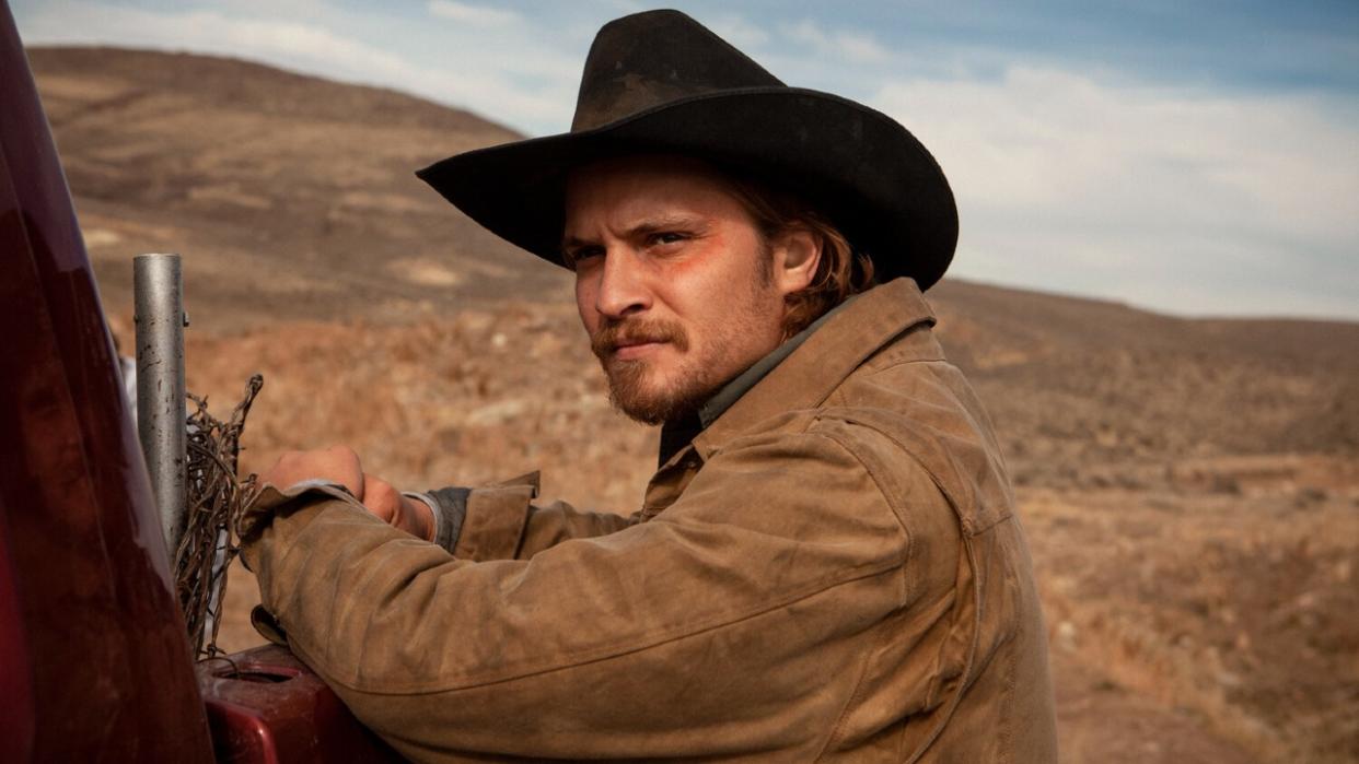  Luke Grimes resting his hands on a truck in Yellowstone. 