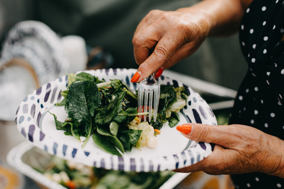 Close up of a senior woman's hands, while eating salad on a paper plate during a social gathering.