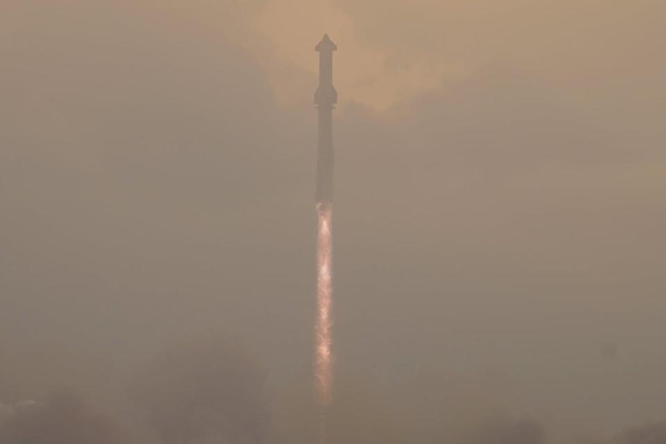 A long, cylindrical rocket rises through the mist.