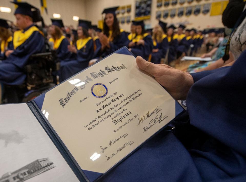 Jon Langione looks at his diploma at Eastern York High School graduation with the class of 2022 in the background.