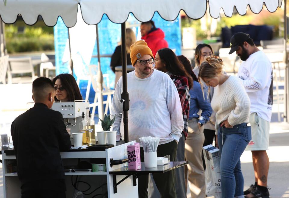 A barista working at an outdoor espresso station with a line of customers