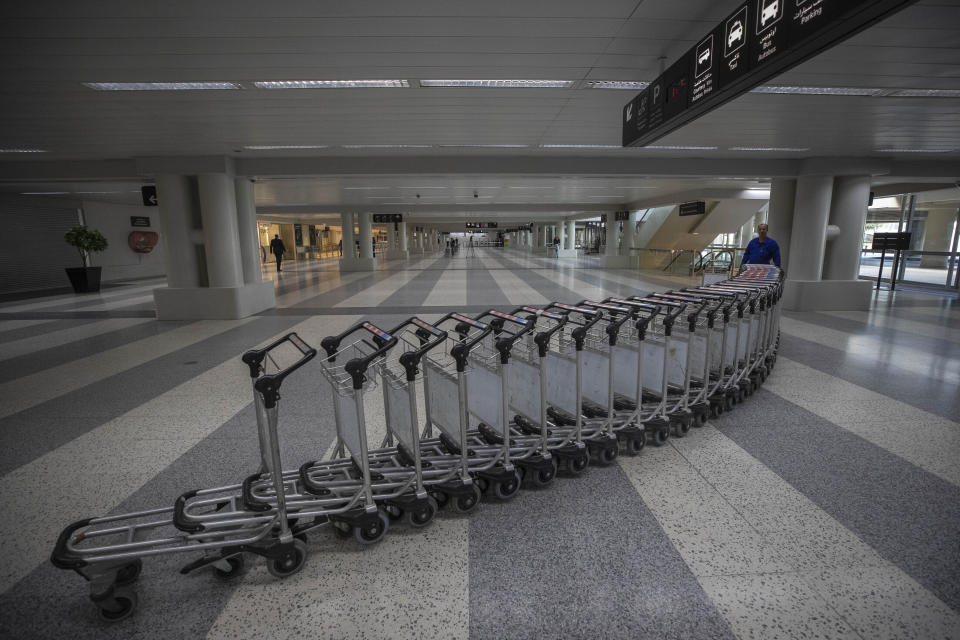 FILE - In this March 19, 2020 file photo, a worker pushes trollies at an empty terminal hall of the Rafik Hariri International Airport, in Beirut, Lebanon. On Wednesday, July 1, 2020, Beirut's airport is partially reopening after a three-month shutdown and Lebanon's cash-strapped government hopes thousands of Lebanese expatriates will return for the summer, injecting badly needed dollars into the sinking economy. (AP Photo/Hassan Ammar, File)