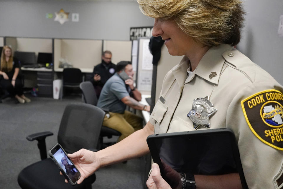 In this Friday, Aug. 13, 2021, photo Sheriff's Police Sgt. Bonnie Busching holds a cellphone as she tests a virtual meeting with mental health professional at the Cook County Sheriff's Office in Chicago. The Cook County Sheriff's department officers are hitting the streets with tablets that can connect people in distress immediately with mental health professionals. And Cook County Sheriff Tom Dart says the Treatment Response Team has been successful bringing calm to the tensest of domestic situations involving people at risk of hurting themselves or others. (AP Photo/Nam Y. Huh)