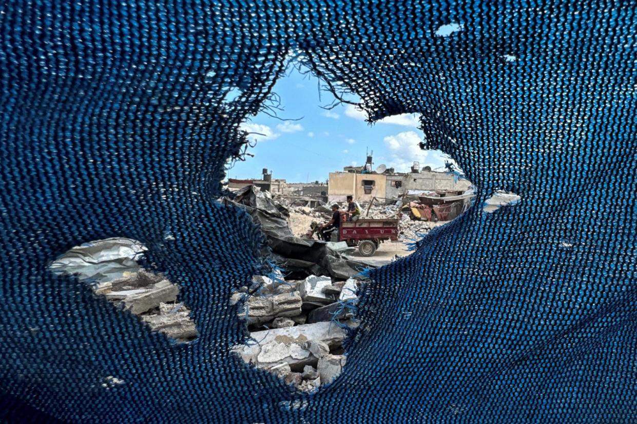 PHOTO: Palestinians, seen through a torn tent, ride a motorized vehicle past the rubble, amid the Israel-Hamas conflict, in Khan Younis, in the southern Gaza Strip, September 16, 2024.  (Mohammed Salem/Reuters)