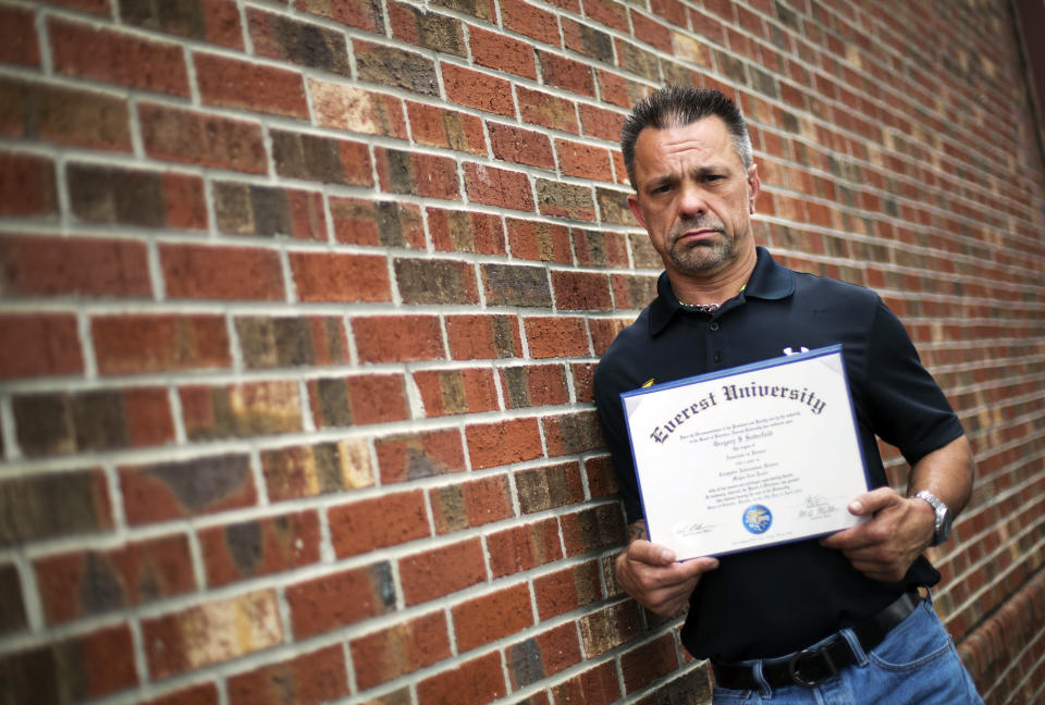 In this March 11, 2016 photo, Shane Satterfield, a roofer who owes more than $30,000 in debt for an associate’s degree in computer science from one of the country’s largest for-profit college companies that failed in 2014, holds his diploma in Atlanta. 