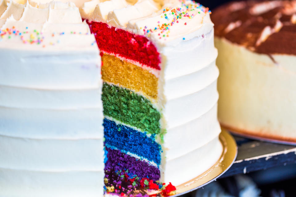 Close up color image depicting a cross section of a freshly baked and iced rainbow layer sponge cake on display at a food market. Room for copy space.