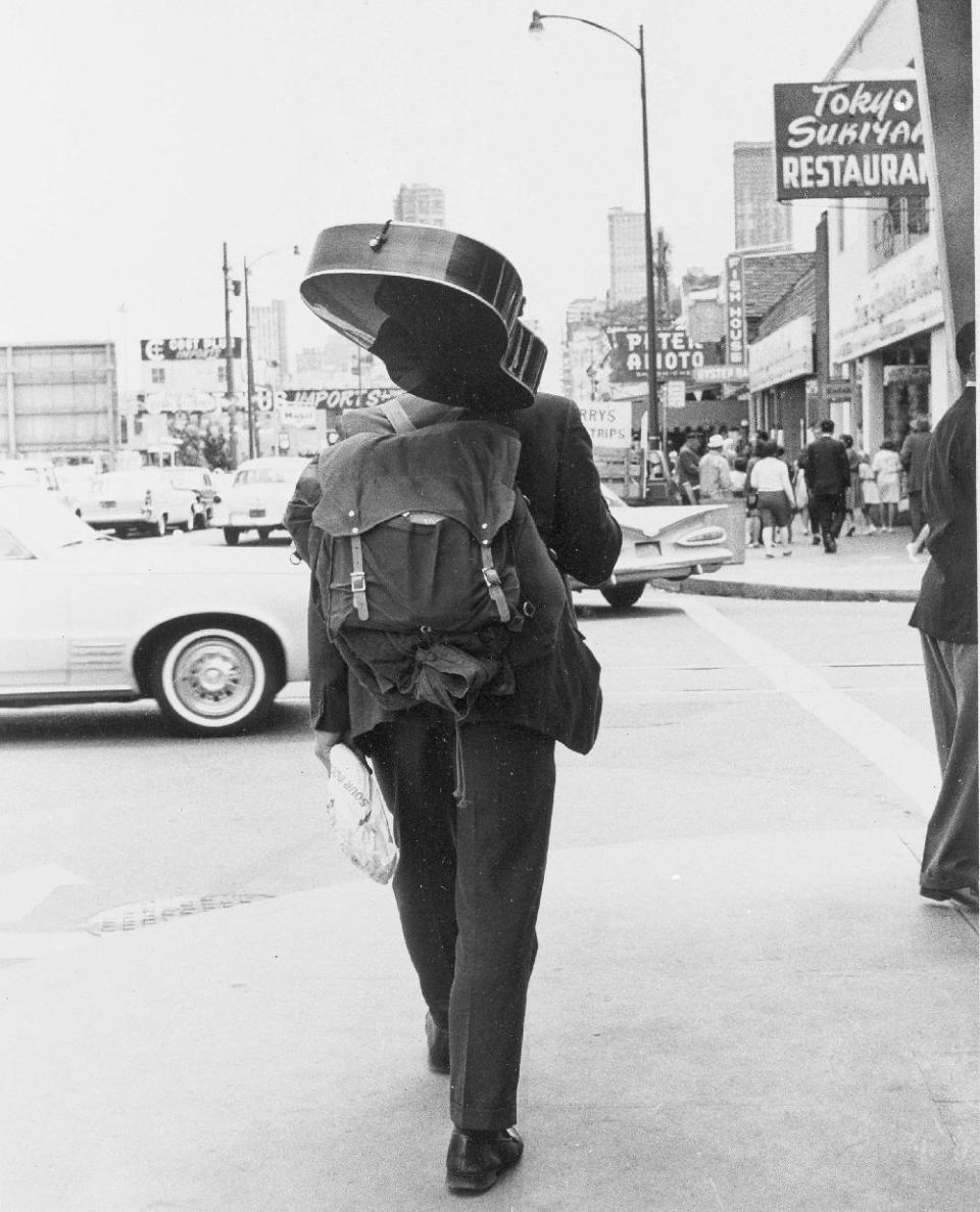 FILE - In this Oct. 16, 1967, file photo, Carrying a loaf of bread, a guitar and a knapsack, a hippie walks down the street away from the Haight-Ashbury district of San Francisco. As the last of the summer weather moves out, so does the influx of young people that came in with it. San Francisco city officials have rejected a permit for a planned free concert intended to mark the 50th anniversary of the famed 1967 Summer of Love in Golden Gate Park that had been planned for June 2017. (AP Photo, File)