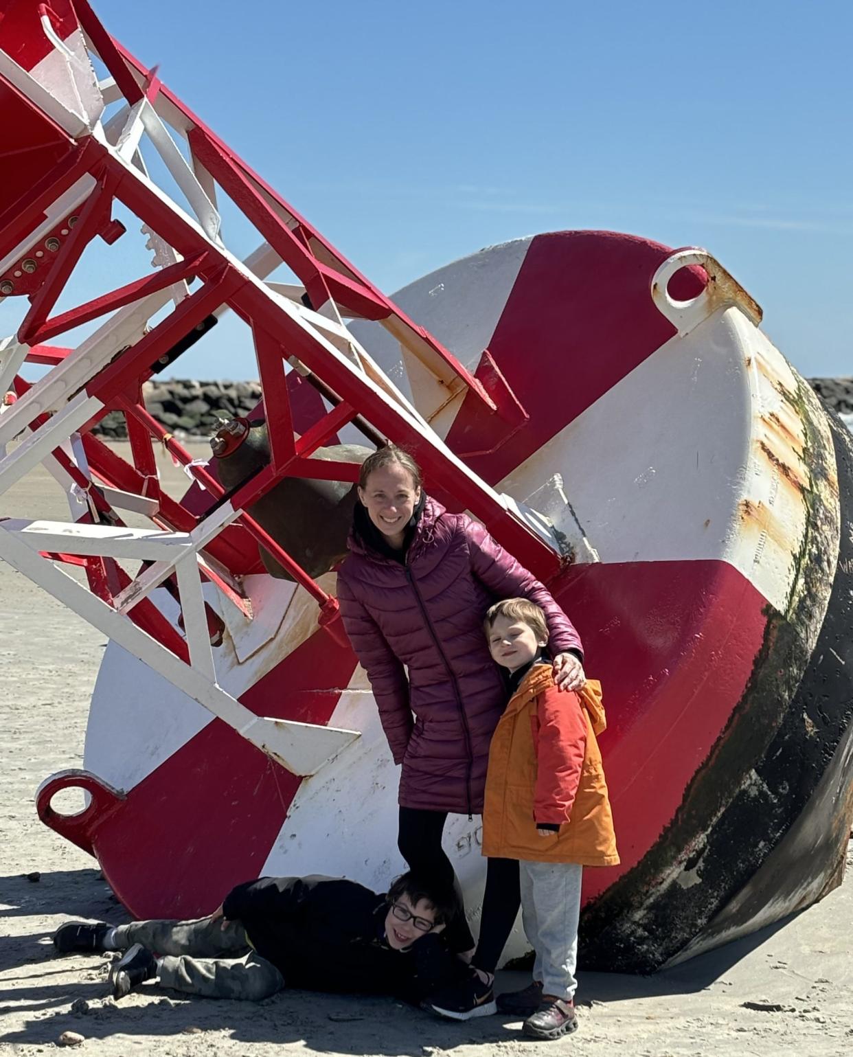 Leah St. Onge and her sons, Arlo, left, and Levy, pose in front of the buoy that washed up onto Wells Beach in Maine, following a storm in early April 2024. The St. Onges were among many who took pictures near the buoy on April 18, 2024.