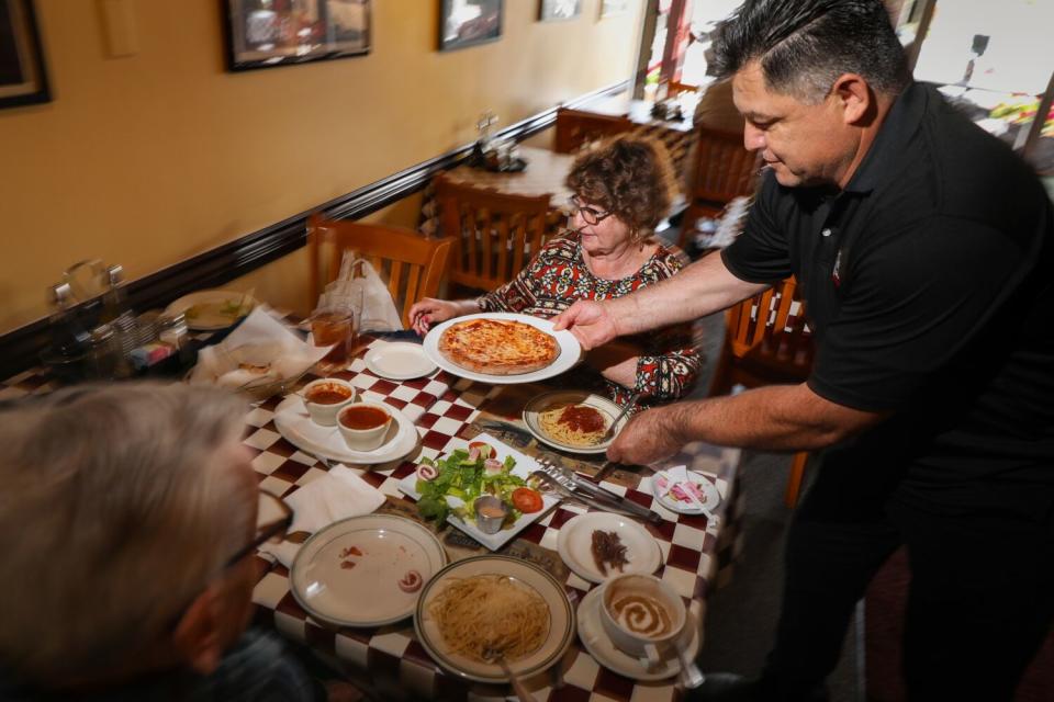 A server delivers a pizza to a table in a restaurant