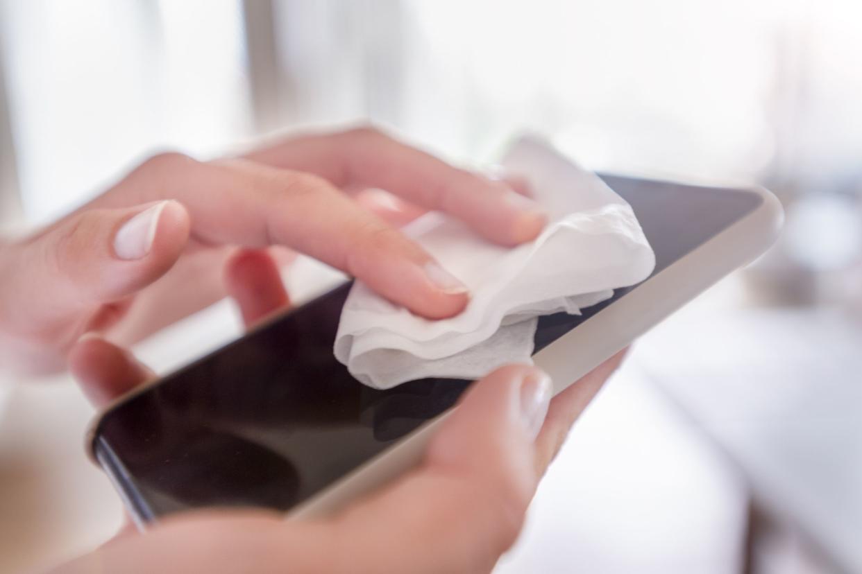 Woman's hands sanitizing her smartphone with a disinfecting cloth being used by one hand to clean the screen, blurred background