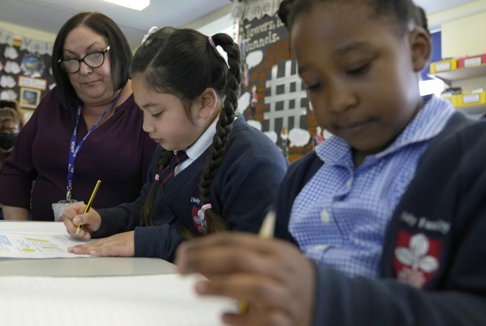 Ruth Monkman year 2 teacher watches over Mia Geraj and Isla as they work during class at the Holy Family Catholic Primary School in Greenwich London, Thursday, May 20, 2021. Before the pandemic, 6-year-old Mia was doing well. But she had a hard time during lockdown, missing her friends and teachers at Holy Family Catholic Primary in southeast London. (AP Photo/Alastair Grant)