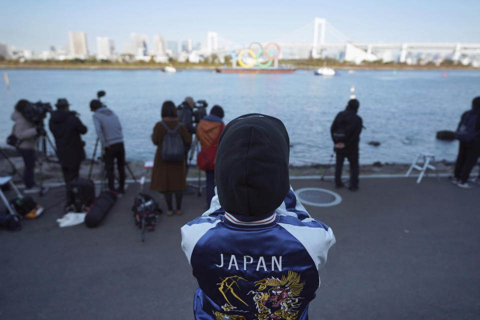 A woman watches at the Olympic Symbol being transported on a barge in the Odaiba section Tuesday, Dec. 1, 2020, in Tokyo. The five Olympic rings are back in Tokyo Bay. They were removed for maintenance four months ago shortly after the Tokyo Olympics were postponed until next year because of the COVID-19 pandemic. (AP Photo/Eugene Hoshiko)