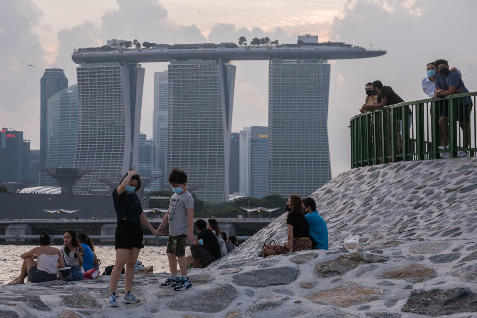 People wearing masks relax on a breakwater with the Marina Bay Sands in the background in Singapore on Sunday, 6 June, 2021. The current phase of social distancing restrictions that are due to  be lifted on 13 June 2021 were enacted after a spike in local COVID-19 cases at the start of May 2021. Some of these restrictions disallow dining in at all food establishments and limit social interaction to groups not larger than 2. (Photo by Joseph Nair/NurPhoto via Getty Images)