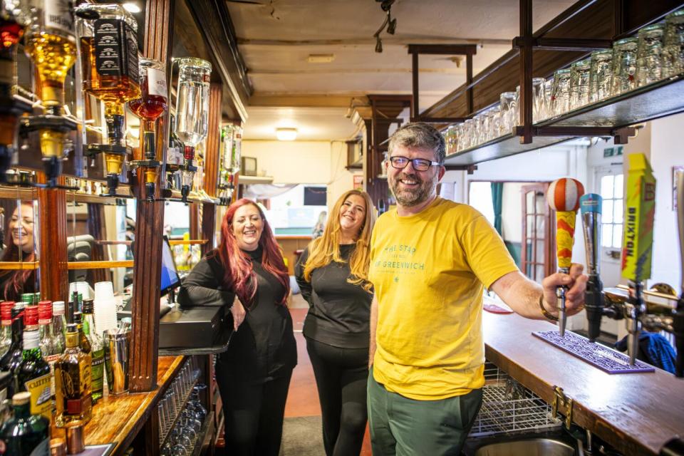 A man and two women stand behind a bar