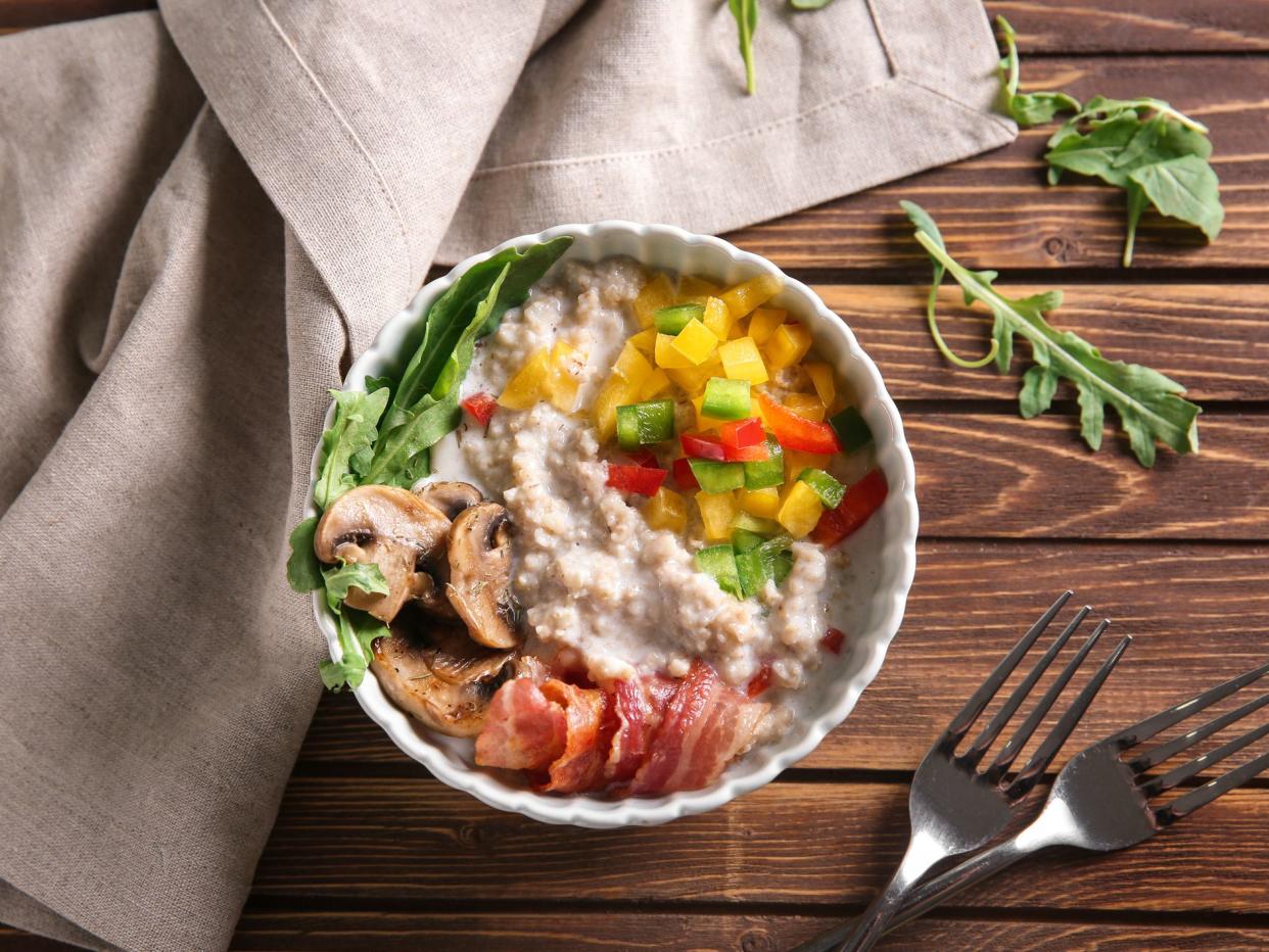 Bowl with tasty oatmeal, fried bacon and vegetables on wooden table