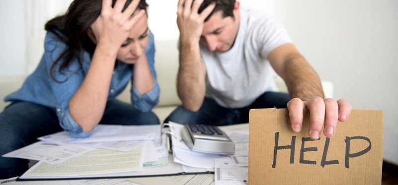 A couple sits perplexed over books and calculator holding up a HELP sign.