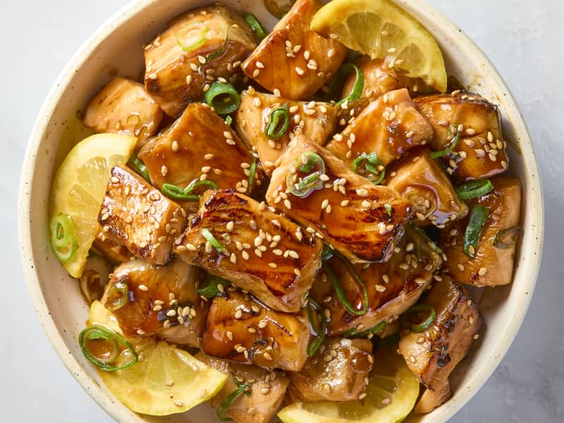 overhead shot of salmon bites in a small bowl, topped with sesame seeds, green onion and lemon wedges