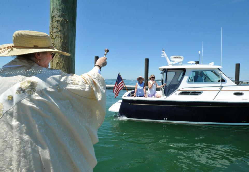 The Rev.  Amy Whitcomb Stemmer of Saint Stephen's Episcopal Church in Boston sprinkles holy water from the A Street pier in Hull on a passing boat during the Blessing of the Fleet in Hull, Saturday, June 25, 2022.
