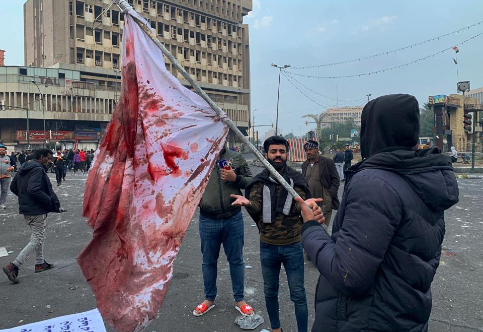 A protester holds a blood-stained flag at the site of a gunmen attack in Baghdad, Iraq, Saturday, Dec. 7, 2019. Gunmen in cars opened fire Friday in Baghdad's Khilani square, killing and wounding scores of people. (AP Photo/Ali Abdul Hassan)