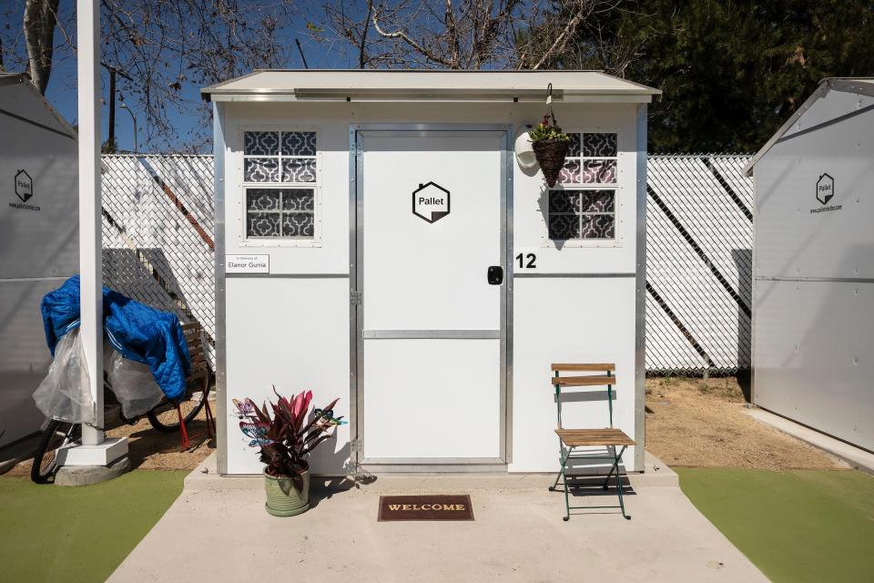 The front of a white tiny home, with a pot of plants and a chair out front.