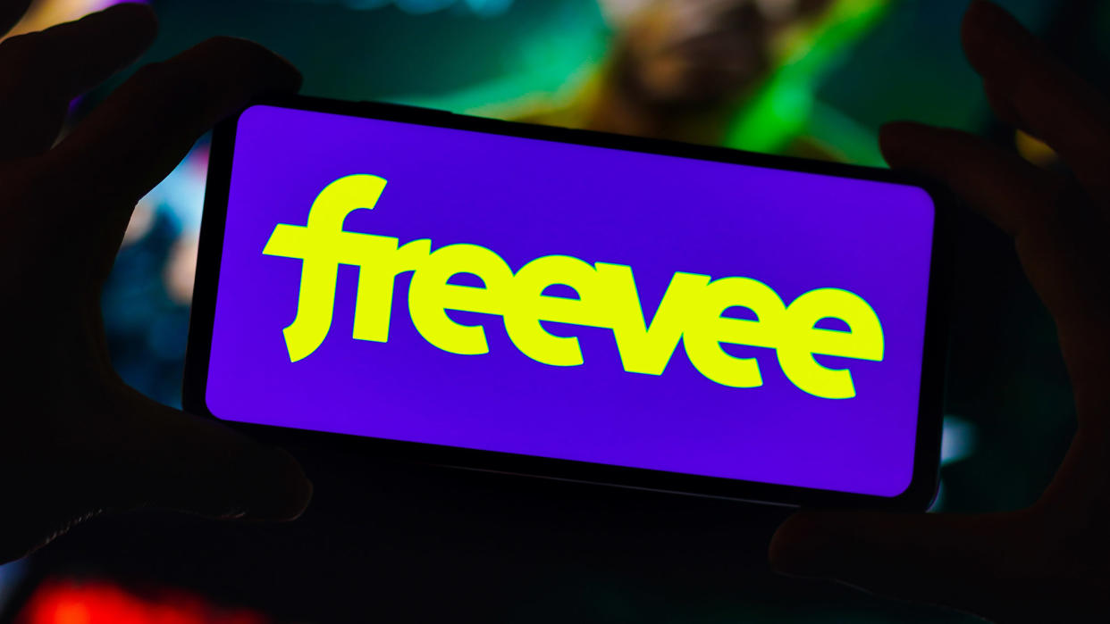  A phone with the 'freevee' logo is held by two hands in the dark. 