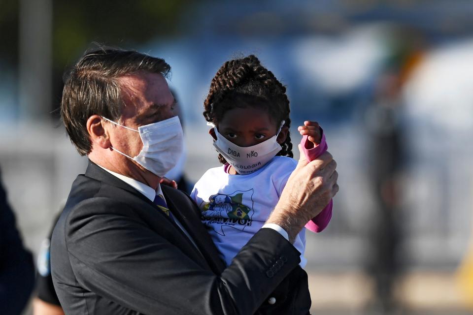 Brazilian President Jair Bolsonaro holds a girl in his arms, both wearing face masks, during the flag-raising ceremony before a ministerial meeting at the Alvorada Palace in Brasilia, on May 12, 2020, amid the new coronavirus pandemic. (Photo by EVARISTO SA / AFP) (Photo by EVARISTO SA/AFP via Getty Images)