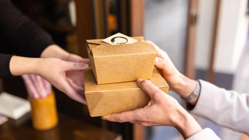 eat out for less: Close-up of a restaurant waiter handing over food packets to a woman customer. Takeaway food during pandemic. Focus on restaurant owner and female customer hands with food boxes.