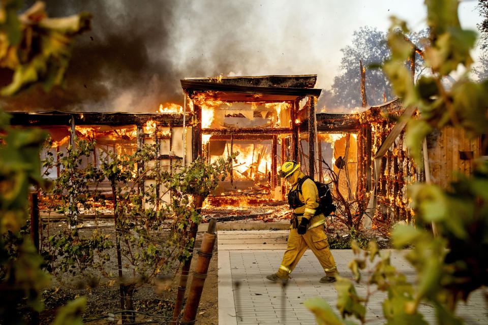 FILE - In this Oct. 27, 2019, file photo Woodbridge firefighter Joe Zurilgen passes a burning home as the Kincade Fire rages in Healdsburg, Calif. California's massive property insurance market is feeling the effects of three straight years of damaging wildfires. Insurers have pulled out of some markets and canceled thousands of policies, forcing regulators to step in and expand a state program that homeowners often turn to as a last resort. (AP Photo/Noah Berger, File)