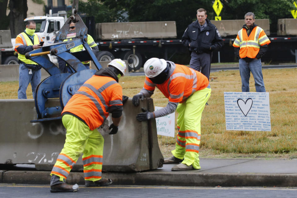 Capitol Police Superintendent Col. Steve Pike, top second from right, and director of The Virginia Department of General Services, Joe Damico, top right, watch as workers install concrete barriers around the statue of Confederate General Robert E. Lee on Monument Avenue Wednesday, June 17, 2020, in Richmond, Va. The barriers are intended to protect the safety of demonstrators as well as the structure itself. (AP Photo/Steve Helber)