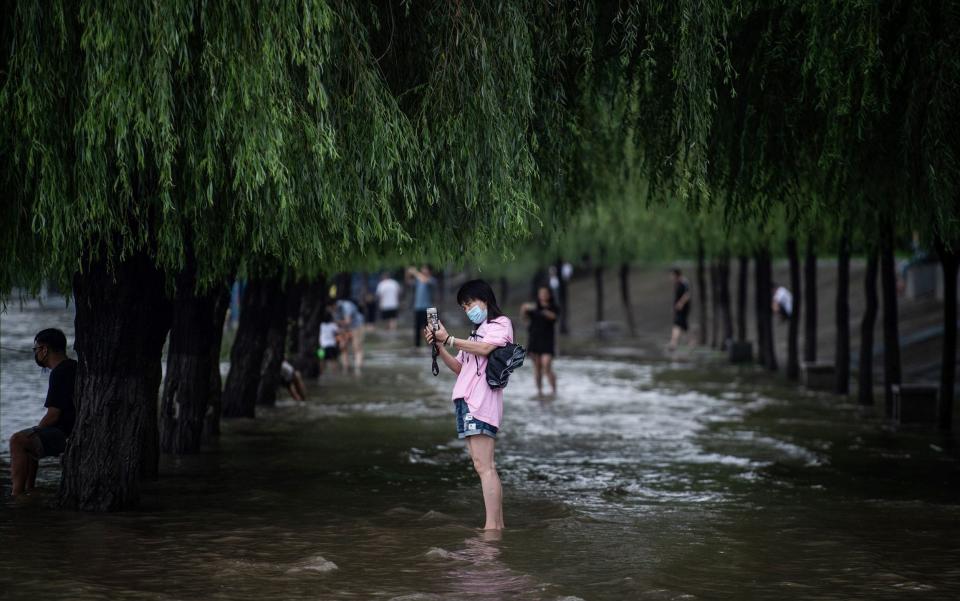 A woman taking photos on a flooded street after heavy rain on the banks of the Yangtze River in Wuhan - AFP