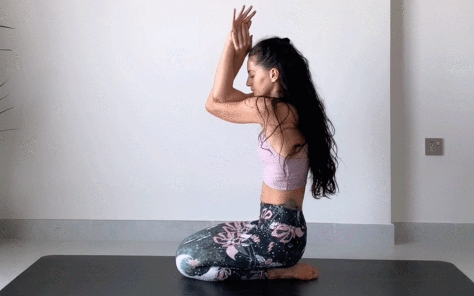 Woman kneeling on a yoga mat practicing a shouder stretch