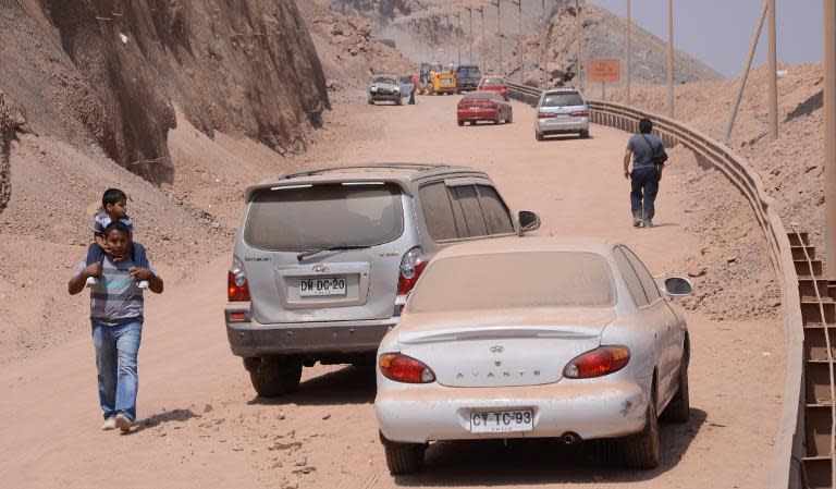 A man carrying his son passes by damaged cars in Iquique, northern Chile, on April 2, 2014 a day after a powerful 8.2-magnitude earthquake hit off Chile's Pacific coast